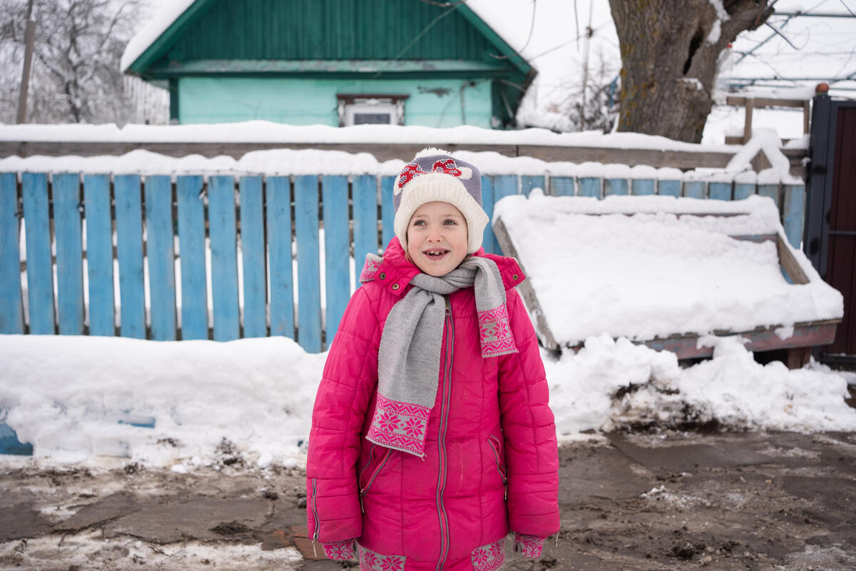 Mariia* is seven years old. She lives in Ukraine with her 39-year-old mother, Viktoriia*, as well as her older brothers – 14-year-old Vsevolod* and 15-year-old Andrii*.

Due to the ongoing conflict in Ukraine, the holiday season is going to look different this year for the family. Before the war, Mariia* went carolling for Christmas and lit sparklers on the street for New Year’s Eve. She helped her mother decorate a Christmas tree and her brother, Vsevolod*, make festive meals including a traditional Ukrainian dish called Kutia containing rice, poppy seeds, and raisins. This year, however, nothing is planned because there isn’t a desire for celebration.

After the conflict escalated at the end of February, the family and a lot of their village community hid in the basement of the local school. In the school’s basement, the family cooked food on a cast-iron stove and talked amongst one another. A few days later, the family returned to their house where, once again, they hid in the basement. Mariia* was frightened by the sound of shelling as well as the lack of light. So, eventually, the family left their village to stay elsewhere in Ukraine. Now, a couple of months later, the family is back in their village, but they had to buy a new house after learning that their old house had been bombed while they were away.

Mariia* is in the third grade. Before the war started, she went to school. Mariia* started going to school early because she was having trouble speaking. Her mother was told that enrolling Mariia* in school would help with her speaking ability. After the war, however, Mariia* hasn’t been able to return to school because the building was bombed and the restoration process is ongoing.

Mariia* likes studying the Ukrainian language, the German language, and mathematics. She loves exercising and reading as well.

Mariia*s mother says that the future is uncertain, but – more than anything – the family wants peace.

Mariia* is taking part in social a
